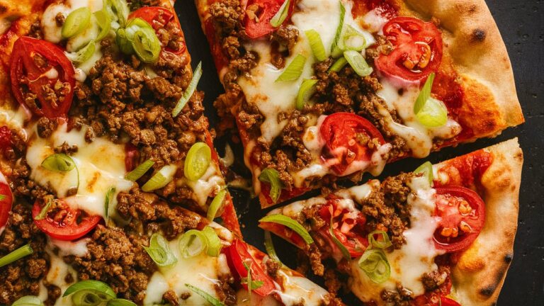 A plate of crispy Mexican pizza, with a crunchy tortilla loaded with seasoned ground beef, melted cheese, and colorful toppings, offering a satisfying and flavorful bite